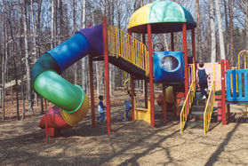 The playground equipment is adjacent to the north end of the parking area.
