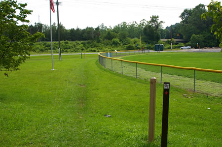 Turn right at the baseball field and walk across the grass on the outside of the fence. If conditions are wet walk down to the paved access road and turn right to follow it.
