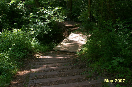 The trail goes down a series of steps and crosses a bridge.