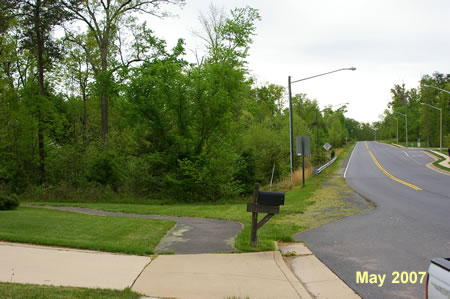 The concrete sidewalk leads into an asphalt trail that turns to the left away from the street.