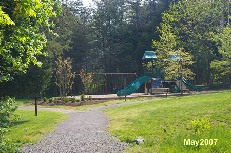 A trail intersects from the right next to a play area. Continue straight on the present trail.